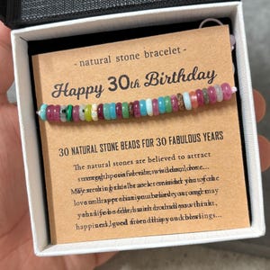 Op de afbeelding: Een kleurrijke natuurstenen armband met kralen in roze, groen, blauw en bruin. De armband wordt gepresenteerd in een geschenkdoos met een kaart met de tekst "Happy 30th Birthday".
