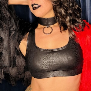 May include: A woman wearing a black leather top with a snakeskin pattern, a black choker with a silver ring, and a red flower on her head.