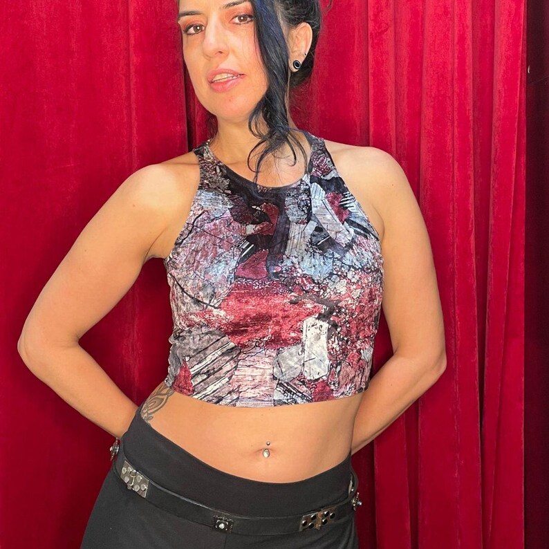 May include: A cropped tank top with a colorful abstract print in shades of red, gray, and black. The top has a halter neckline and a fitted silhouette.