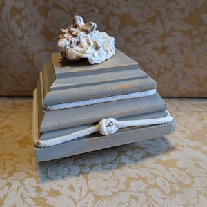 May include: A gray wooden box with a seashell on top. The box is decorated with white rope.