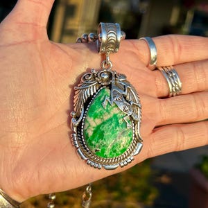 May include: A silver pendant necklace featuring a green stone and a silver lizard design. The necklace has a silver chain.