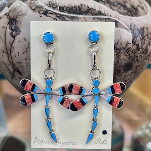 Op de afbeelding: Zilveren libellen oorbellen met turkoois en ingelegde vleugels in zwart, rood en wit. De oorbellen hebben een pin met een turkoois steen en de handtekening van de kunstenaar. Unieke sieraden.