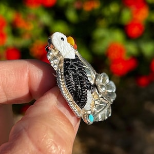 May include: A silver and turquoise eagle pin with black jet inlay. The eagle is perched on a branch with a flower.