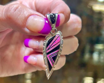 May include: A silver pendant with a black onyx top and a geometric design of pink and black lines. The pendant has a teardrop shape with a decorative edge.