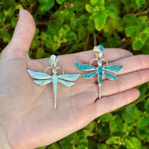 May include: Two sterling silver dragonfly pendants with opal inlay. One pendant has a blue and green opal inlay, the other has a white opal inlay.