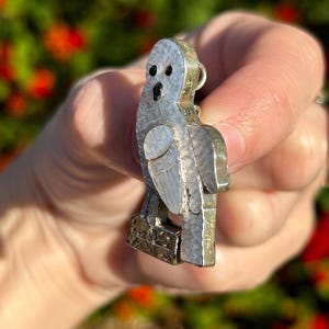 May include: A silver owl pendant with a mother of pearl inlay. The owl is perched on a branch with its wings spread out.