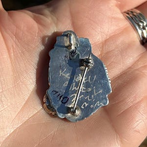 May include: Silver pendant with a detailed design and a pin back. The back of the pendant is inscribed with "7/10" and "Wesley".
