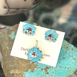 May include: A jewelry set featuring a pendant and matching earrings. The pieces have a turquoise flower design with a central geometric pattern in red, black, and white. The set is displayed on a white card with text.