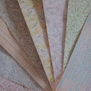 May include: A selection of textured wallpaper samples in a fan arrangement. The samples feature floral, dotted, and striped patterns in beige, yellow, green, and blue hues. The samples are arranged in a fan shape.