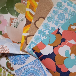 May include: A collection of vintage wallpaper samples featuring various patterns and colours. The samples include a floral design with blue and white accents, a geometric pattern with brown and orange accents, and a floral design with pink and green accents.