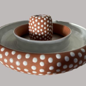 May include: A terracotta-colored ceramic dish with white polka dots. The dish has a smaller, white ceramic bowl inside, also with white polka dots.