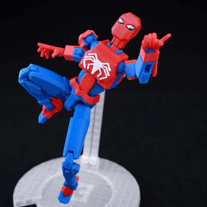 May include: A posable action figure of a character with a red and blue suit, featuring a white spider emblem on the chest. The figure is captured in a dynamic mid-air pose, supported by a clear plastic stand with a circular base on a black background.