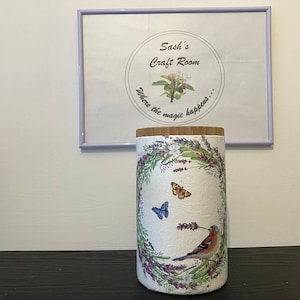 May include: A white ceramic jar with a wooden lid, decorated with a floral wreath, butterflies, and a bird. The jar has the text "Sash's Craft Room, Where the magic happens..." on the lid.