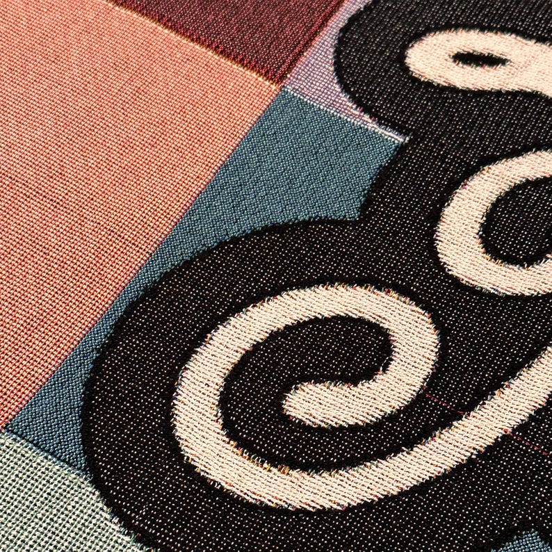 Close up of colorful woven cotton Dog Mom throw blanket featuring retro checkerboard design.