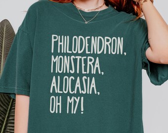 May include: Dark green t-shirt with white text: "PHILODENDRON, MONSTERA, ALOCASIA, OH MY!". The shirt is a comfortable, casual style, perfect for plant lovers. The text is in a bold, sans-serif font.