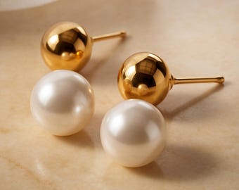 May include: A pair of stud earrings featuring two polished gold spheres and two smooth white spherical pearls. Each earring consists of a metal post and a round element, showcasing a reflective metallic finish and a classic pearl luster.