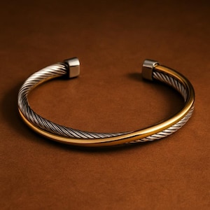 May include: A two-tone cuff bracelet with a twisted silver and gold design. The bracelet has a silver twisted cable design on the top half and a gold band on the bottom half. The ends of the bracelet are silver.