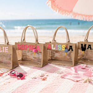 May include: Four rectangular jute tote bags with clear plastic windows and top handles. Each bag features personalized block lettering in various colors: KYLIE in pink, SOPHIA in neon pink, ALISSA in multicolored letters, and MARIE in black, with ice cream charms.
