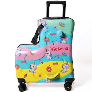 May include: A colorful rolling suitcase with a unicorn theme. The suitcase is decorated with unicorns, donuts, and bows in shades of blue, pink, yellow, and green. The name "Victoria" is printed on the side. It has a black handle and wheels.