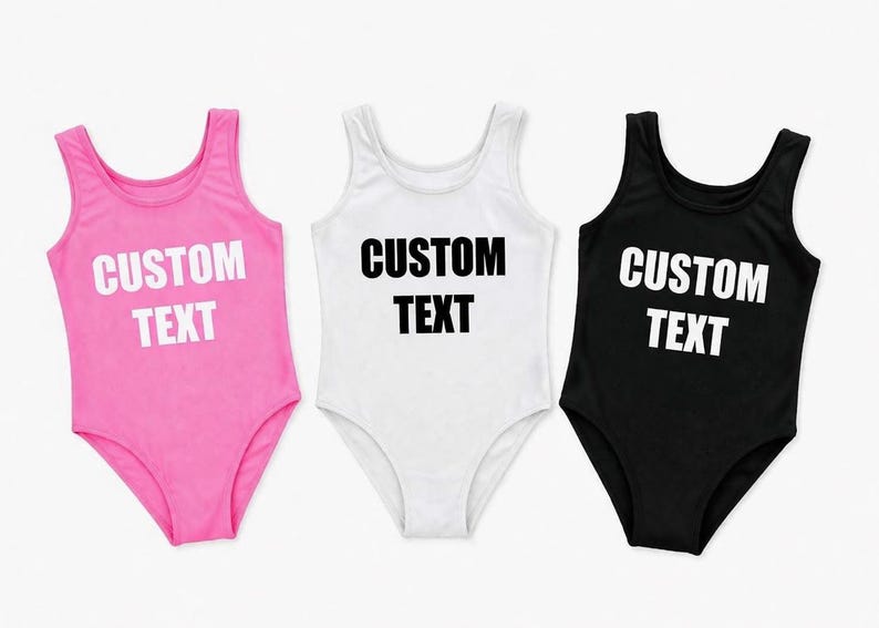 May include: Three custom text bodysuits in pink, white, and black. Each bodysuit has a scoop neck and is sleeveless. The words "CUSTOM TEXT" are printed in bold white letters on the pink and black bodysuits and in black on the white bodysuit.