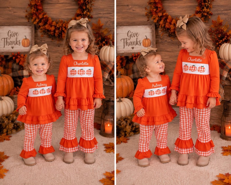 May include: Two matching orange long-sleeve tops with white smocked panels featuring embroidered pumpkins and the names Aubrey and Charlotte, paired with orange and white gingham print bell-bottom pants with ruffled hems and tan hair bows.