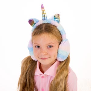 May include: A young girl wearing a pink shirt and unicorn earmuffs with a rainbow and iridescent design. The earmuffs are soft and fluffy.