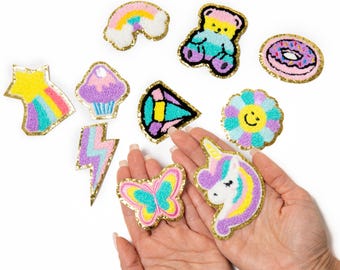 May include: A collection of colorful punch needle patches featuring a rainbow, a teddy bear, a donut, a shooting star, a cupcake, a lightning bolt, a diamond, a flower with a smiley face, a butterfly, and a unicorn, all with gold trim.