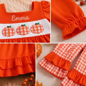 May include: An orange long-sleeve top featuring a white chest panel with three embroidered orange and white gingham pumpkins and the name Emma in white script. The garment includes ruffled sleeve cuffs and a double-tiered ruffled hemline.