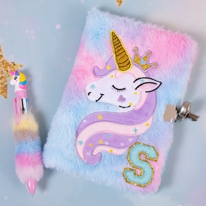 May include: A blue and pink fuzzy notebook with a purple and pink unicorn with a gold crown and a gold letter "S" on the front. The notebook has a lock and key.