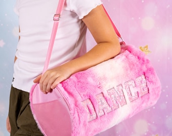 May include: A pink and white faux fur duffel bag with a glittery "DANCE" design. The bag has a pink adjustable shoulder strap.