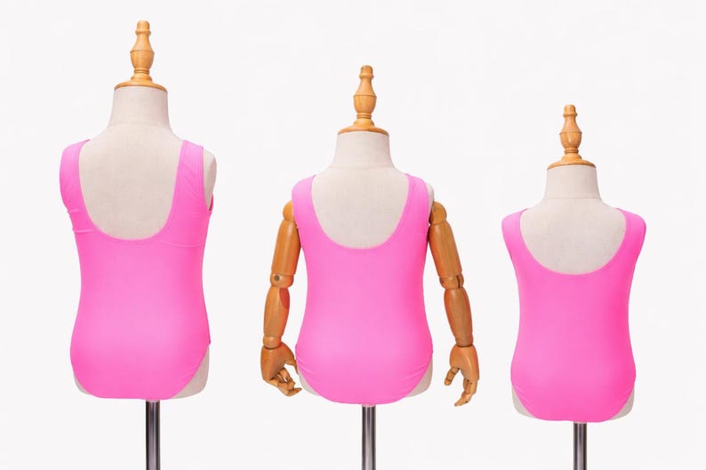 May include: Three pink swimsuits displayed on mannequins. The swimsuits have a scoop back design and are a vibrant shade of pink. The mannequins are on metal stands against a white background. The swimsuits are likely for children.
