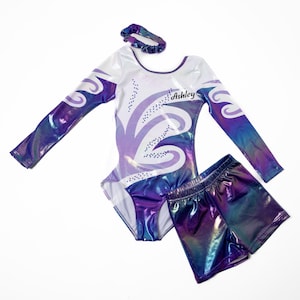May include: A purple and white leotard with long sleeves and a swirl design. The leotard has rhinestones and the name "Ashley" written on the front. A matching pair of purple shorts with a iridescent finish is also included.
