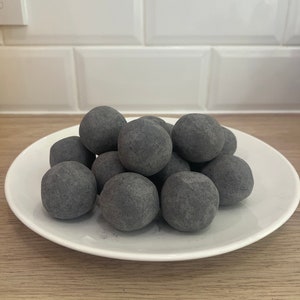 May include: A white plate with a pile of small, round, black charcoal balls.