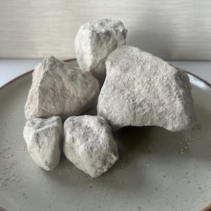 May include: A collection of five irregular, chalky white rocks with a rough, porous texture. The stones vary in size and shape, featuring jagged edges and a matte finish. They are clustered together, displaying a natural, unrefined appearance.