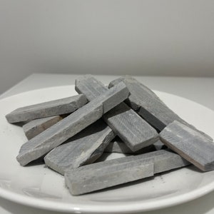 May include: A pile of gray slate pencils on a white plate. The pencils are rectangular and have a rough texture.