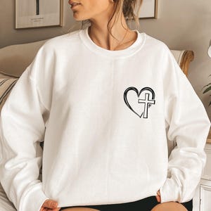 May include: White sweatshirt with a black heart and cross graphic.