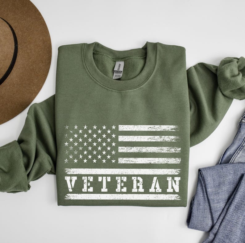 May include: A green sweatshirt with a white distressed American flag and the word "Veteran" printed on the front.