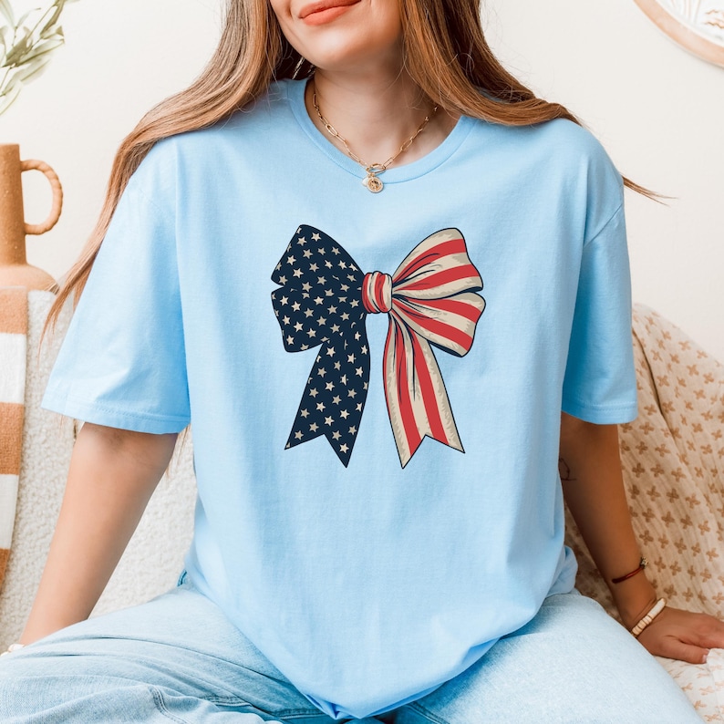 Peut inclure: Un t-shirt bleu clair avec un n&oelig;ud rouge, blanc et bleu. Le n&oelig;ud est con&ccedil;u pour ressembler &agrave; un drapeau am&eacute;ricain.