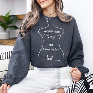 K&ouml;nnte beinhalten: Dunkelgraues Sweatshirt mit wei&szlig;em Text, der lautet: "Happy Birthday Jeffrey and I'm on the list". Der Text befindet sich innerhalb einer wei&szlig;en Umrisszeichnung eines Torsos. Die Person h&auml;lt einen wei&szlig;en Becher.