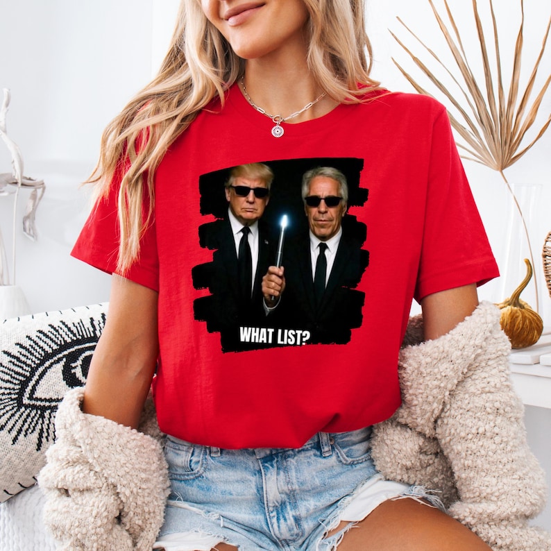 K&ouml;nnte beinhalten: Rotes T-Shirt mit einer Grafik von zwei M&auml;nnern in schwarzen Anz&uuml;gen und Sonnenbrillen, von denen einer einen leuchtenden Zauberstab h&auml;lt. Der Text "WHAT LIST?" steht unter dem Bild. Das Shirt ist aus weichem Material.