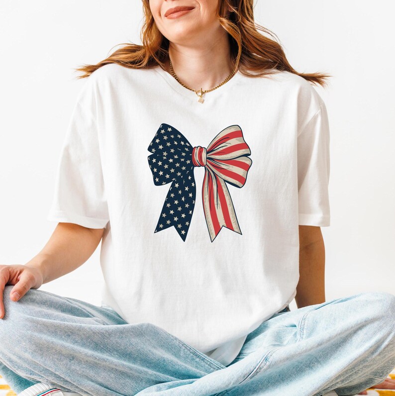 Peut inclure: T-shirt blanc avec un n&oelig;ud rouge, blanc et bleu imprim&eacute; sur le devant. Le n&oelig;ud est con&ccedil;u pour ressembler &agrave; un drapeau am&eacute;ricain.