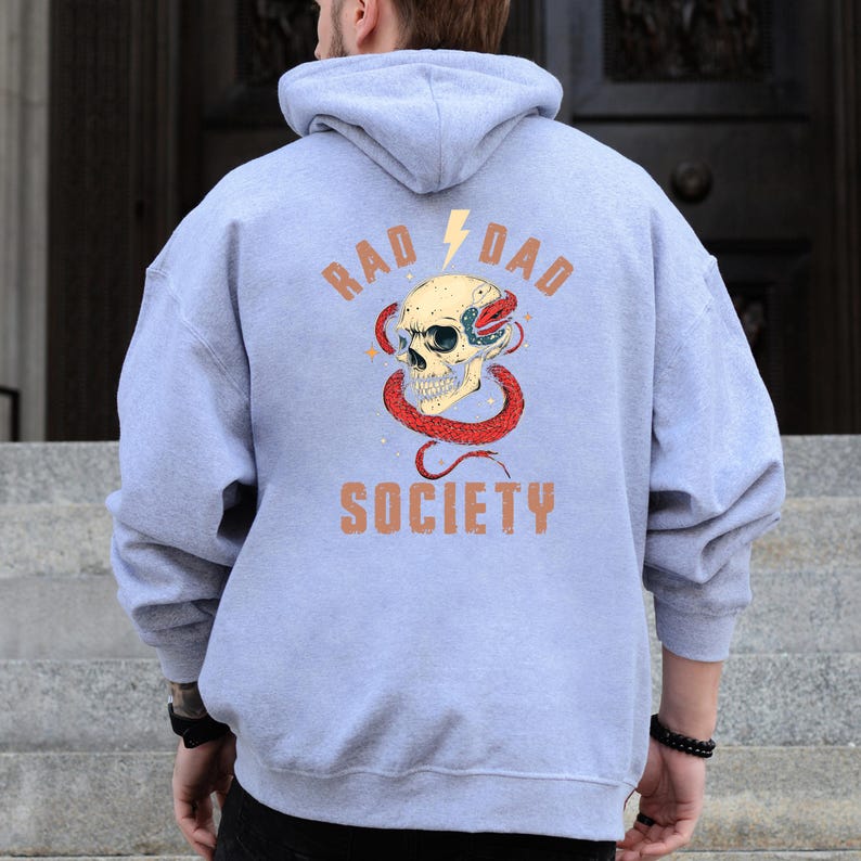 May include: A light blue hooded sweatshirt with a graphic print of a skull with a snake wrapped around it. The text "Rad Dad Society" is printed on the back of the sweatshirt.