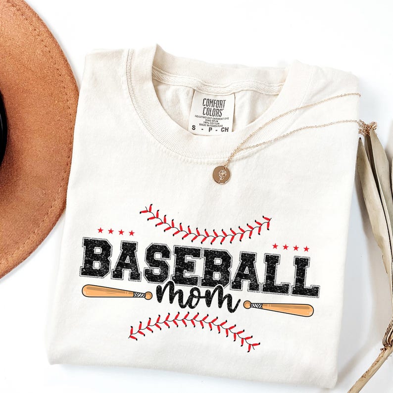 May include: A beige t-shirt with a black and white graphic that says "Baseball Mom" with a baseball bat and red stitching. The shirt has a tag that says "Comfort Colors".