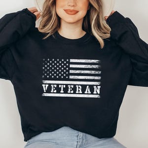 May include: Black sweatshirt with a white distressed American flag and the word "VETERAN" printed on it.