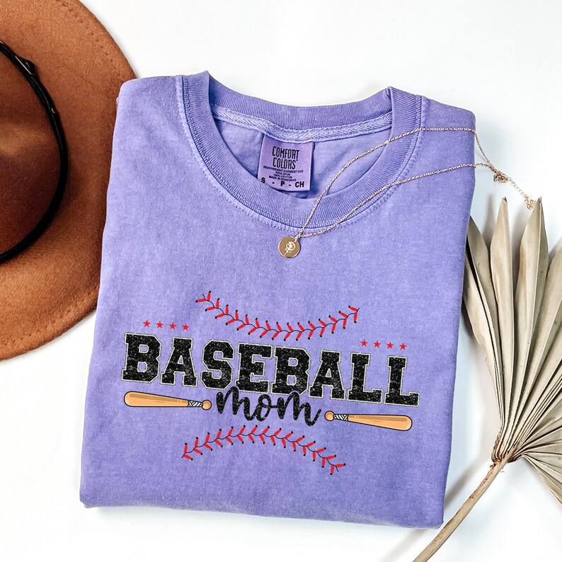 May include: A purple t-shirt with a baseball graphic and the text "Baseball mom" printed on it. The shirt is made of a soft, comfortable material.