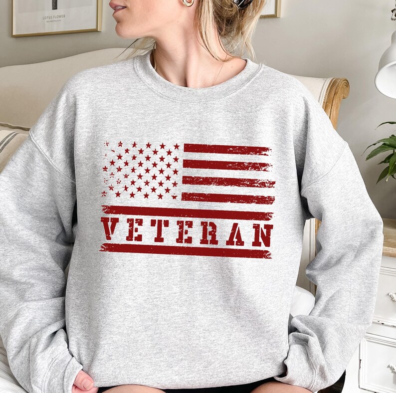 May include: Gray sweatshirt with a red, white, and blue distressed American flag and the word "VETERAN" in red.