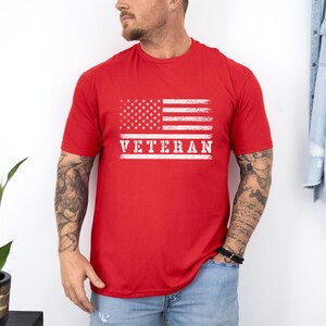 以下が含まれることがあります： 赤いTシャツに、くたびれたアメリカ国旗と白い文字で「Veteran」と書かれている