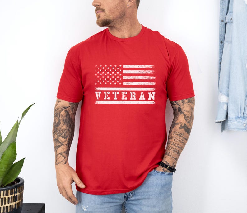 以下が含まれることがあります： 赤いTシャツに、くたびれたアメリカ国旗と白い文字で「Veteran」と書かれている
