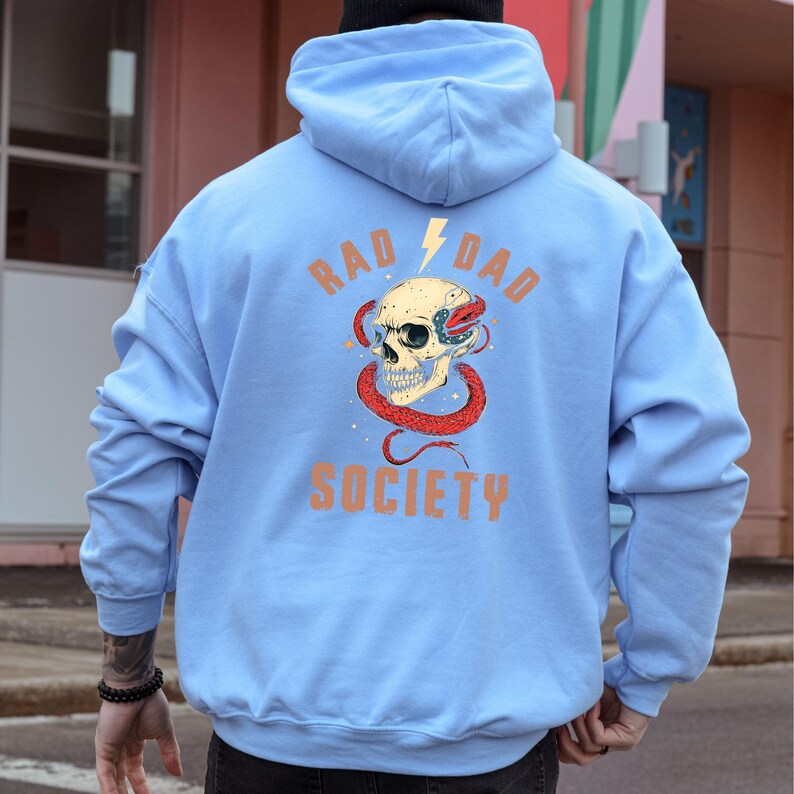 May include: A light blue hoodie with a graphic of a skull with a snake wrapped around it. The text "RAD DAD SOCIETY" is printed on the hoodie.
