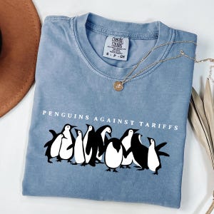 May include: A light blue t-shirt with a graphic of penguins and the text "PENGUINS AGAINST TARIFFS".
